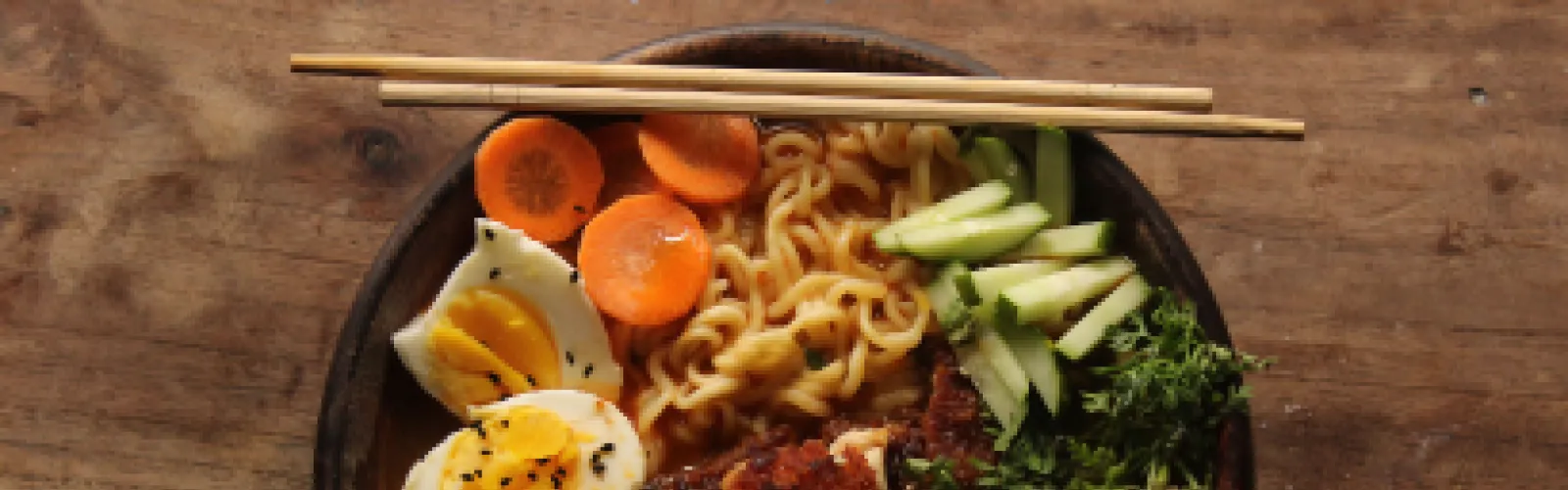 A bowl of ramen with carrots, cucumbers, egg, and meat added.