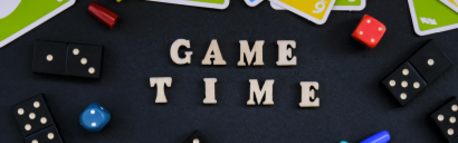 Game Time written in wooden letters on a black table surrounded by various game items like UNO cards and dominos.