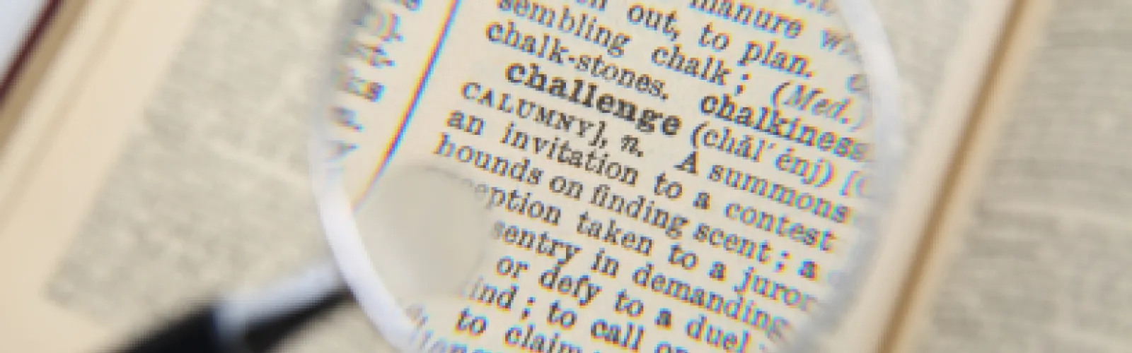 magnifying glass over the dictionary definition of a challenge.