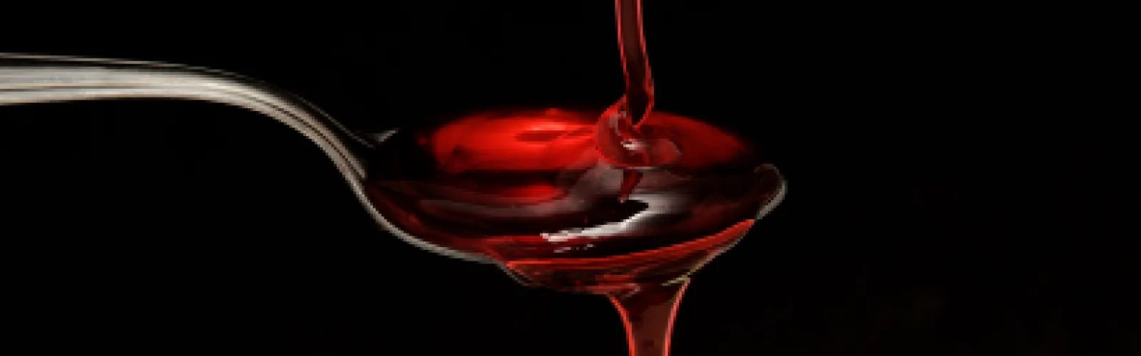Fake corn syrup blood on a metal spoon against a black background