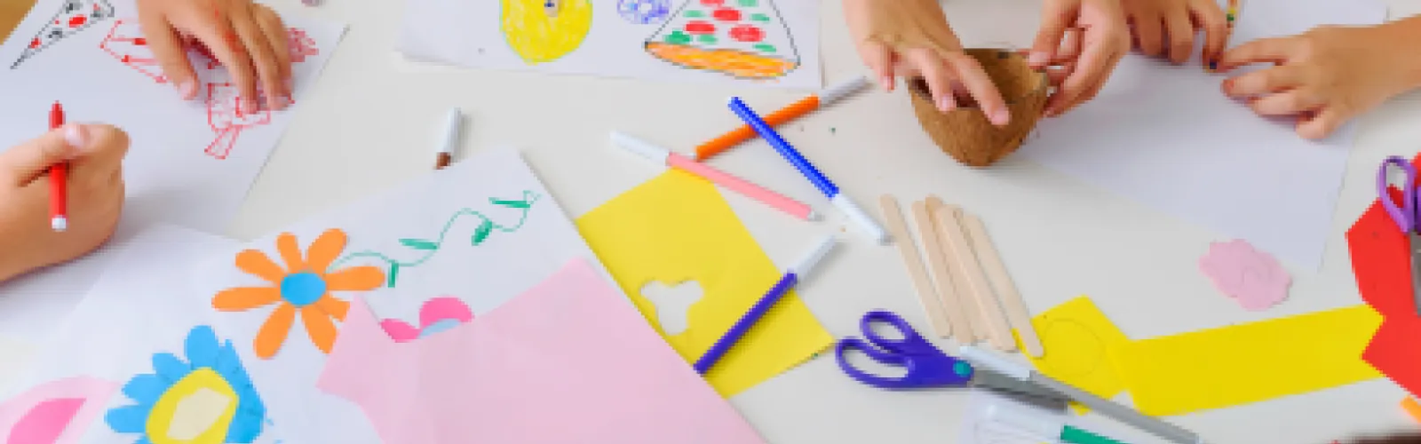 various colorful paper crafts on a white table, hands reaching in to work on projects