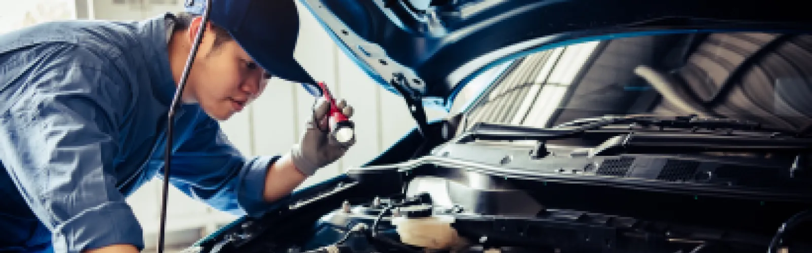 a young mechanic working on a car holding a flashlight